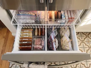 An organised French-door freezer drawer with clear bins labelled Use first and Treats in the top basket.