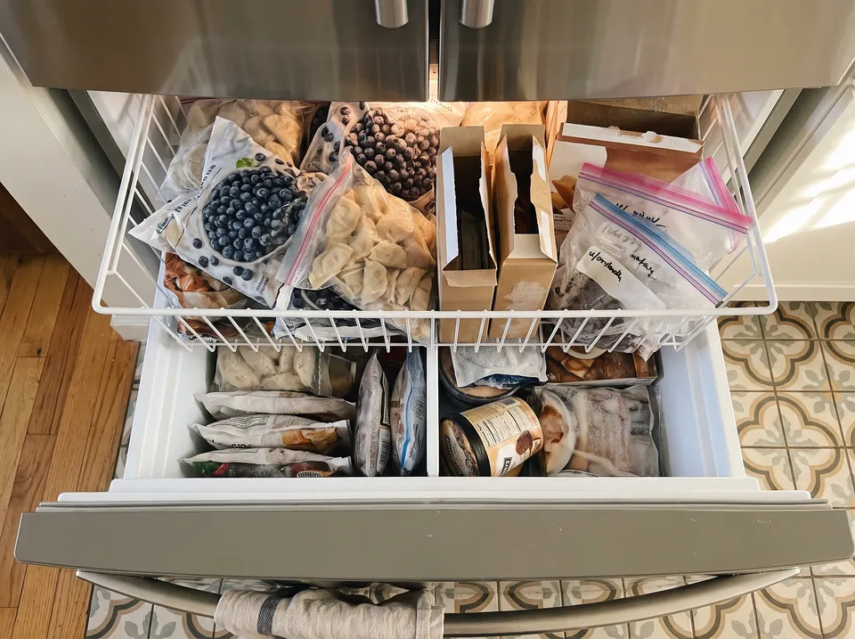 A French-door freezer drawer before organizing: bulk bags slumped on their sides, open boxes of ice-cream bars and loose zip bags, nothing visible at a glance.